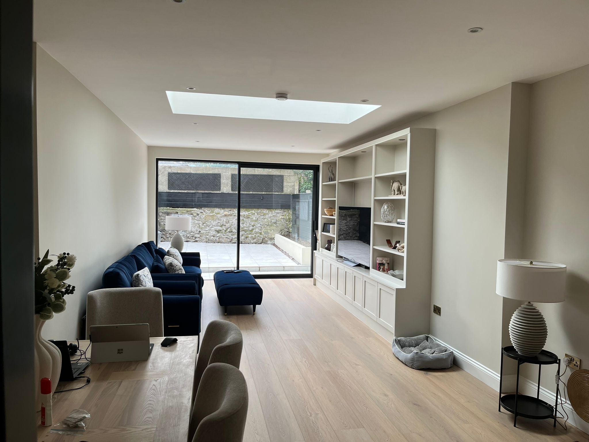 Open-plan living extension with white built-in shelving, blue sofa, skylight and sliding doors to courtyard