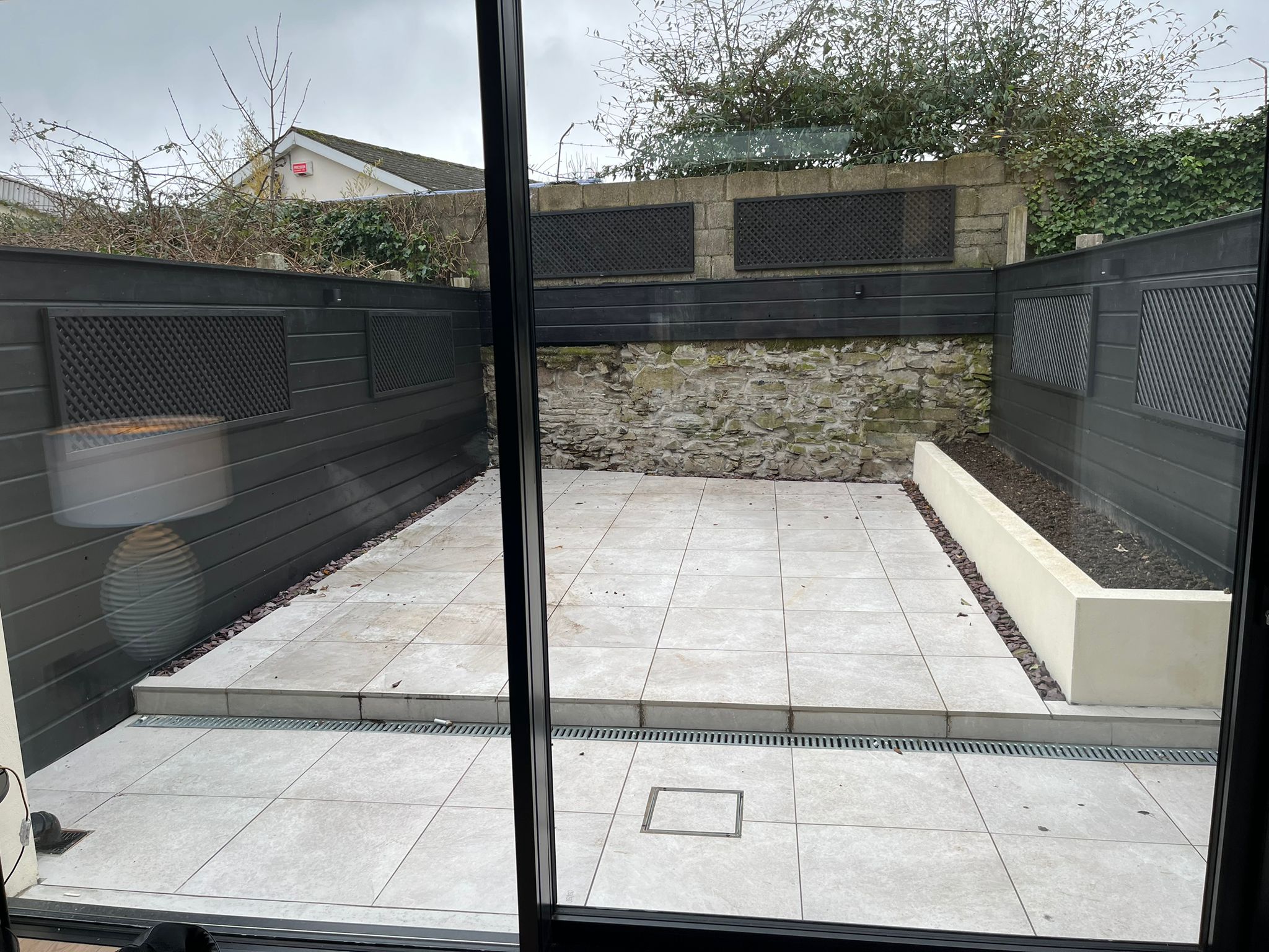 Completed courtyard viewed through large sliding glass doors with dark fence panels and stone boundary wall