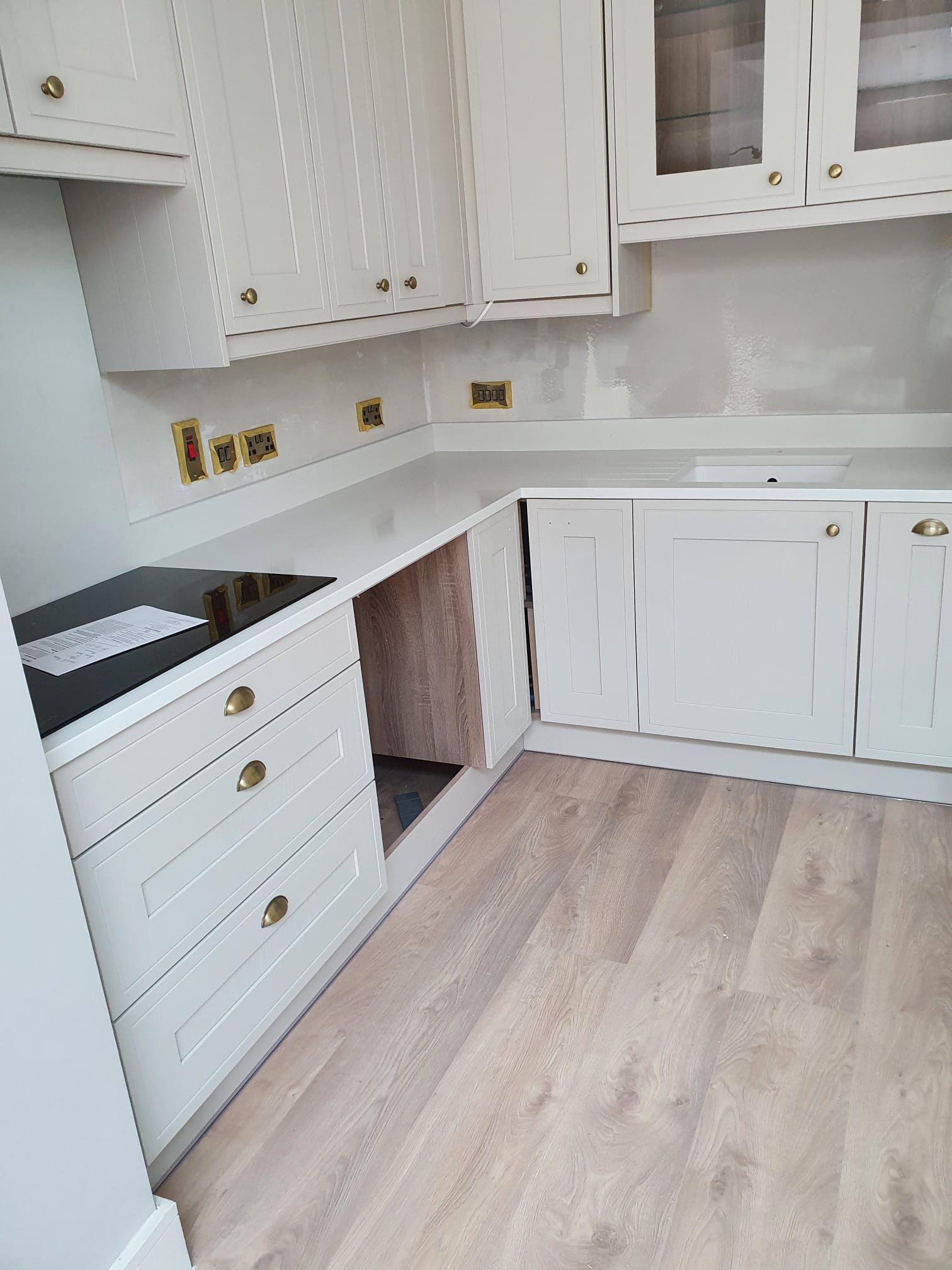 White shaker kitchen installation with brass handles and light wood flooring